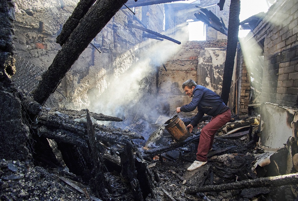 Residente de Kharkiv tenta apagar um fogo num edifício residencial destruído por bombardeamentos